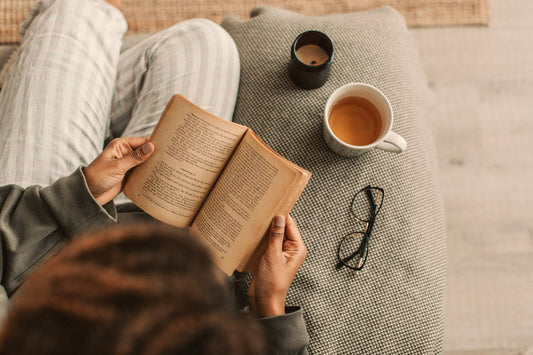 Person reading a book with a cup of tea indoors, a self care story about starting over